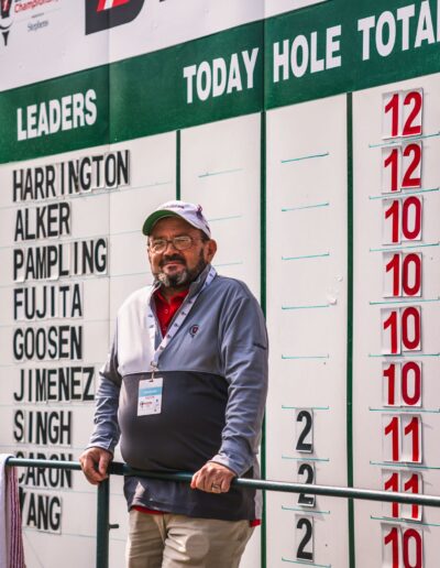 A scoring volunteer standing in front of the tournament leaderboard